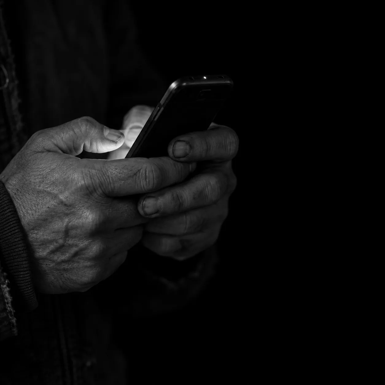 Worn hands holding a phone, the screen the only light, one red notification light lit.